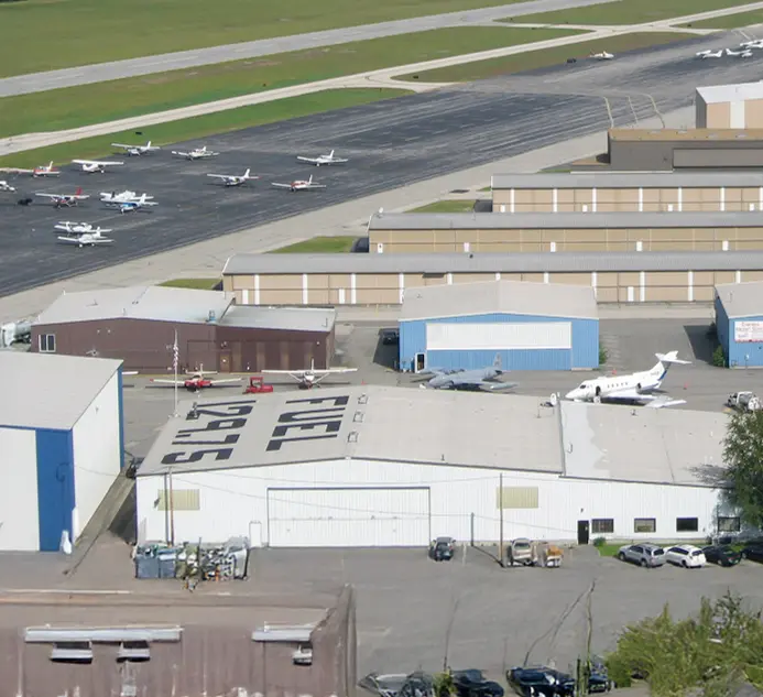 Aerial view of a bustling small airport showing hangars, parked airplanes, and a fuel station with pricing.