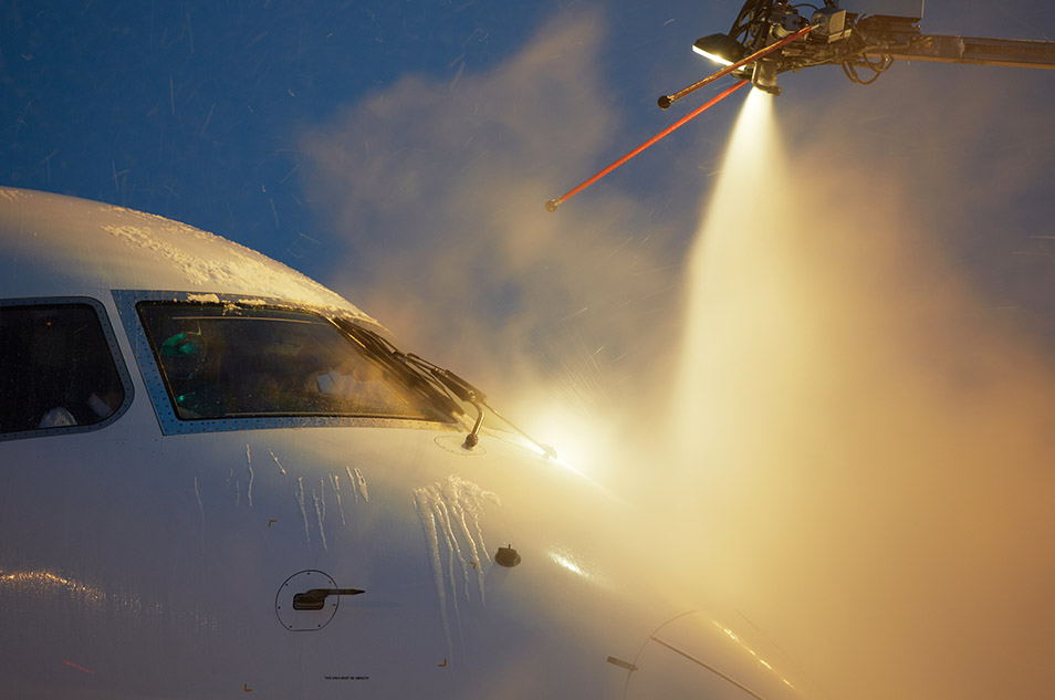 Airplane undergoing deicing process at night, sprayed with anti-ice fluid to remove snow and prevent ice formation.