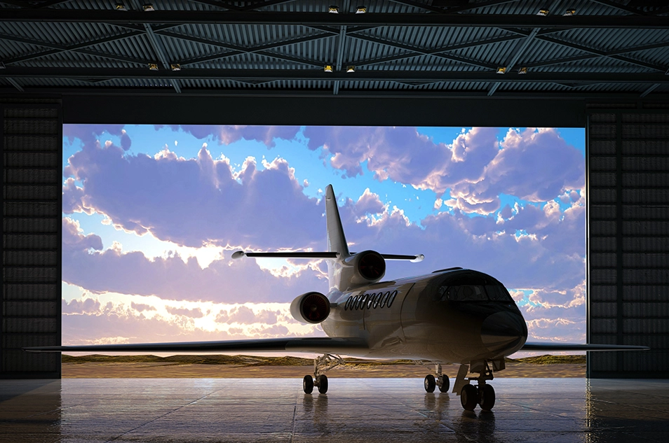 Private jet park inside hangar under a vibrant sky with clouds.