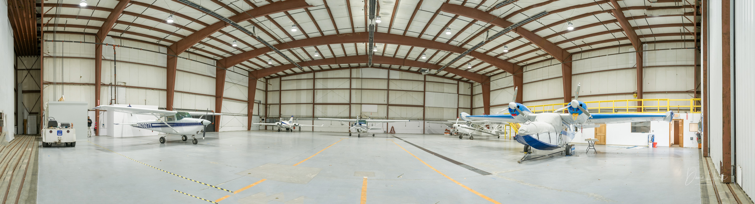 Inside view of a spacious aircraft hangar with several small planes parked.
