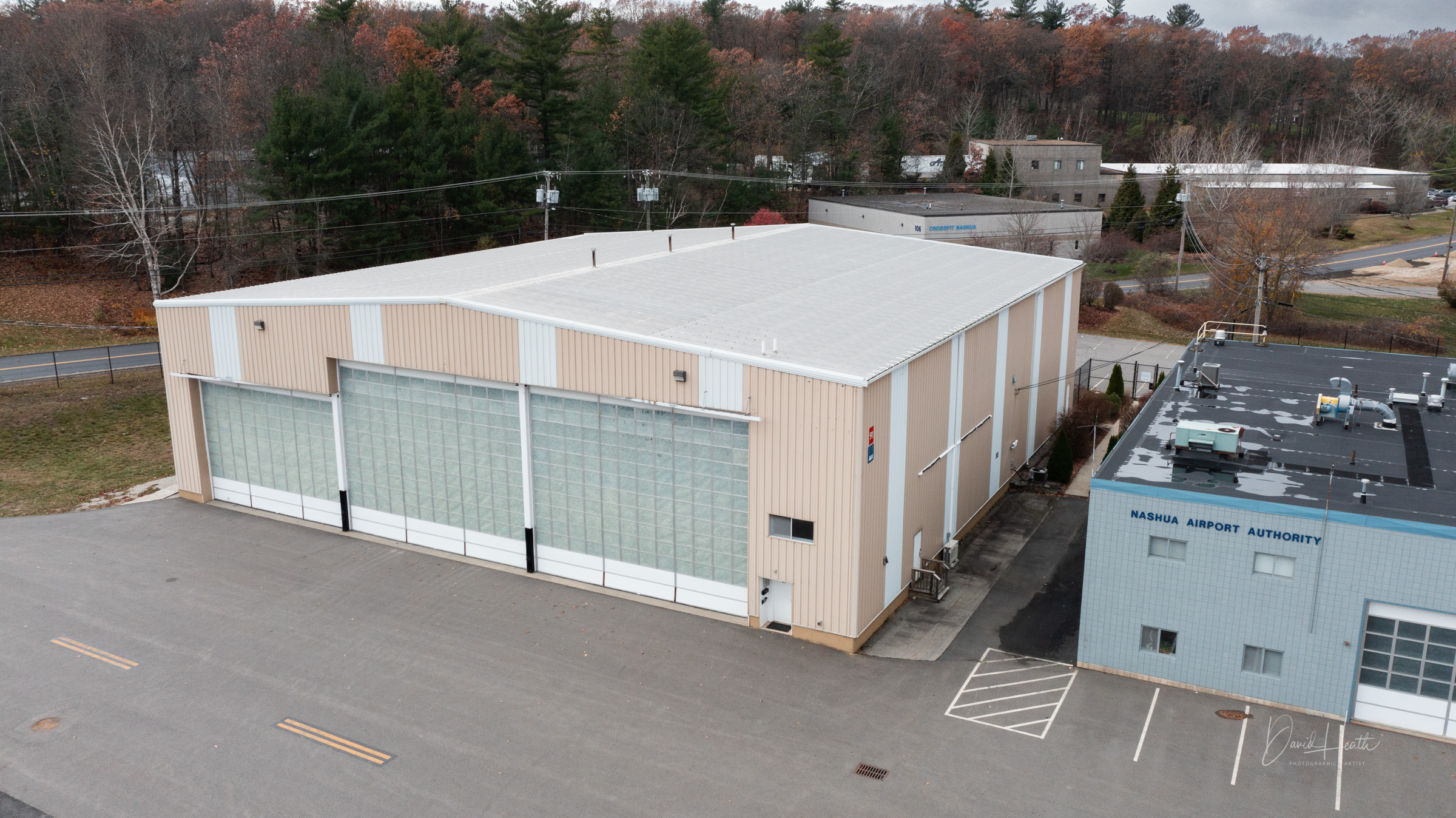 Aerial view of Nashua Airport Authority building and hangar surrounded by trees and a road.
