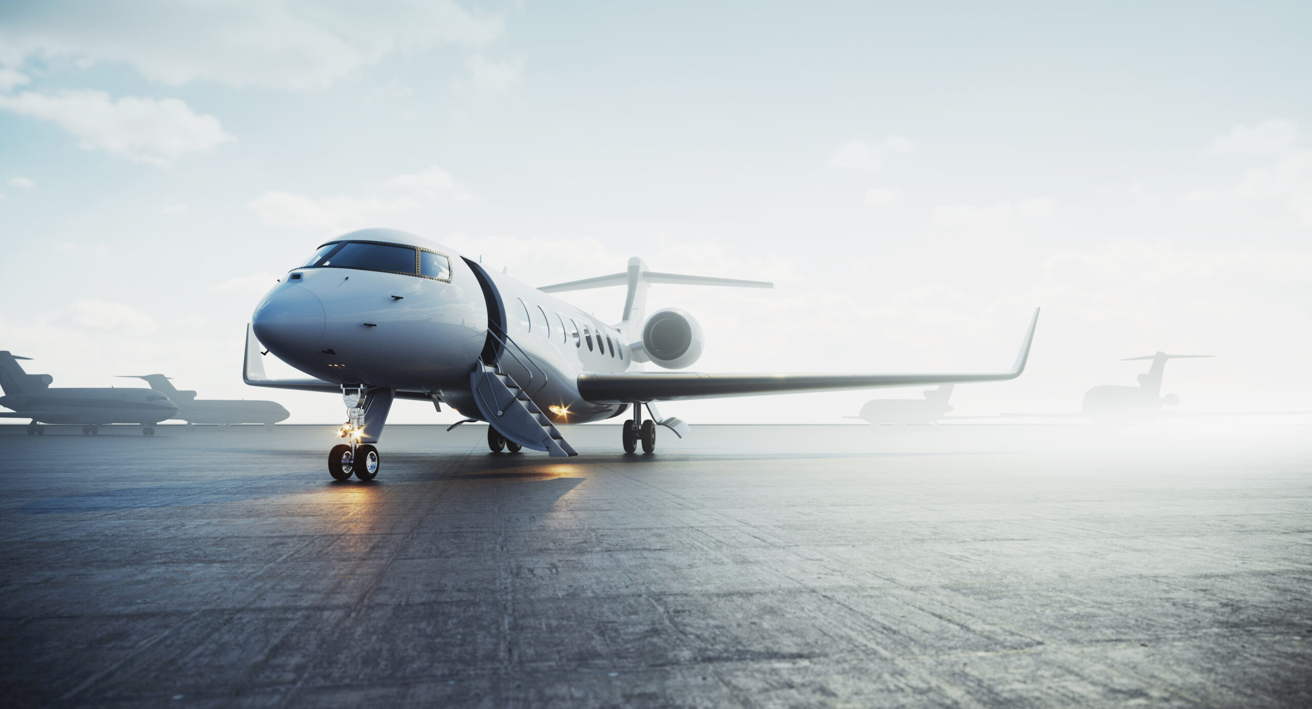 Private jet on tarmac with open stairway, lit landing gear, and a clear blue sky in the background.