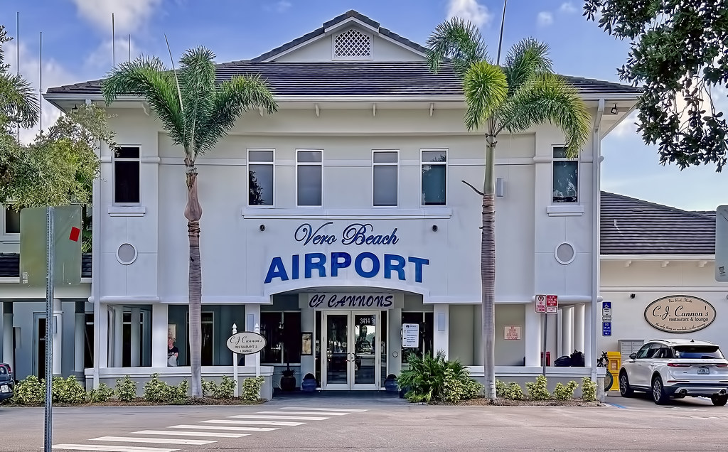 Vero Beach Airport entrance with palm trees, featuring CJ Cannon's Restaurant. Bright, sunny day with clear skies.