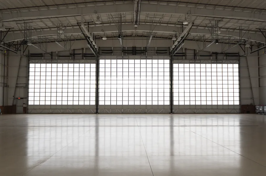 Spacious empty aircraft hangar interior with large closed doors and a high ceiling structure.